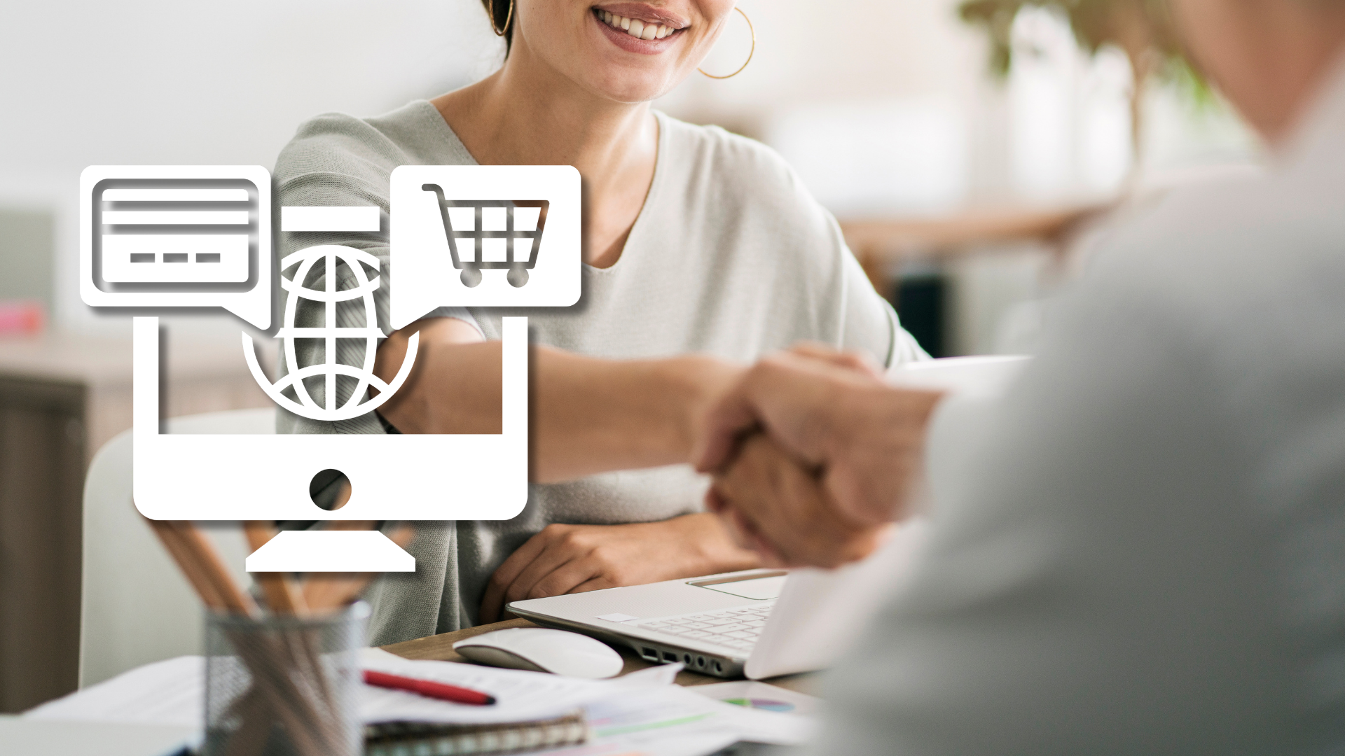 Apretón de manos ante un escritorio con portátil e icono blanco de tienda online – contratar a un especialista en e-commerce